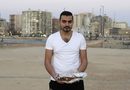Хамед Махмуд, 30, държи риба на грил в Александрия, Египет. Хамед е от Кайро и споделя, че любимите му ястия са риба на грил и морски дарове. Когато посещава Александрия, той обича да се храни с приятели на брега на морето