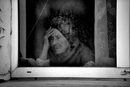 Възрастна жена гледа през прозореца на своя дом близо до центъра на Мариупол.