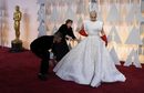 Лейди Гага бе избрала пищна сребристобяла рокля, комбинирана с червени гумени ръкавици. Роклята е дело на Алая. Гага беше единодушно избрана за най-зле облечената знаменитост на тазгодишната церемония. 
На снимката: Асистенти оправят роклята на певицата на 87-та церемония по връчването на наградите "Оскар"