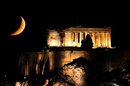 Луната се вижда зад осветения храм на Партенона, разположен на хълма Акропола в центъра на Атина, Гърция.