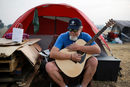 Кели Бойер свири на китара пред палатката си до супермаркет. Кели е принуден да живее на палатка, след като къщата му е била унищожена от пожарите в Парадайз, Калифорния, САЩ.