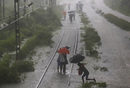 Пътници довършват пътуването си пеш по наводнен железопътен коловоз заради обилен валеж в Мумбай, Индия.