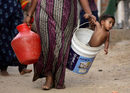 Жена носи сина си в кофа край общински резервоар за вода в покрайнините на Ченай, Индия.