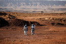 От вратата на експедиционната база, на няколко крачки вляво, минава автономен роувър. На няколко крачки вдясно е разположен масив от слънчеви панели. Пейзажът е скалист, хълмист, оцветен в червено. Наподобява Марс.<br /><br />Тук, в кратера Рамон в пустинята на Южен Израел, екип от шестима души - петима мъже и една жена, симулират какво е да живееш около месец на Червената планета.