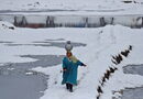 Жена със стомна за вода върви през заснежено поле в покрайнините на Шринагар.