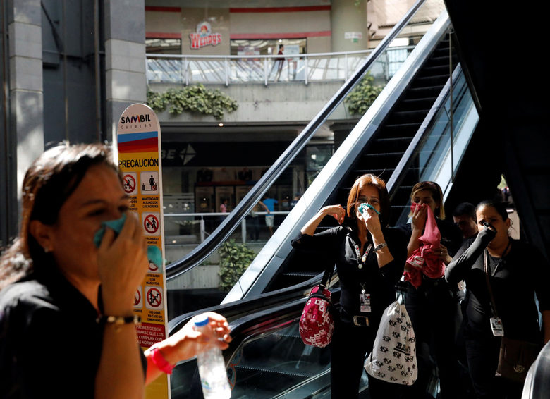 Хора покриват лицата си, за да се предпазят от сълзотворен газ в търговски център в Каракас, Венецуела