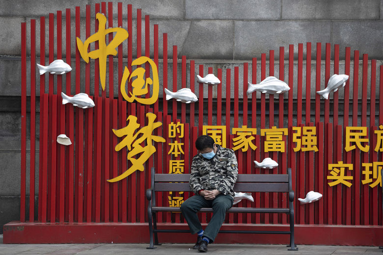 Жител в Ухан седи на пейка, зад която пише "Китайска мечта".