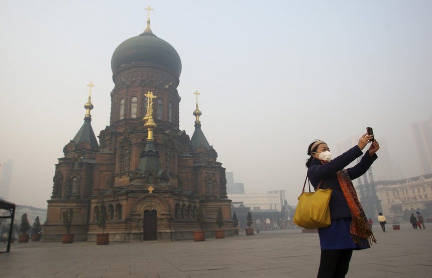 Жена, с маска на лицето срещу мръсния въздух, си прави селфи с мобилния си телефон на площада пред църквата Св.София Харбин, в Харбин, провинция Хъйлундзян, Китай.