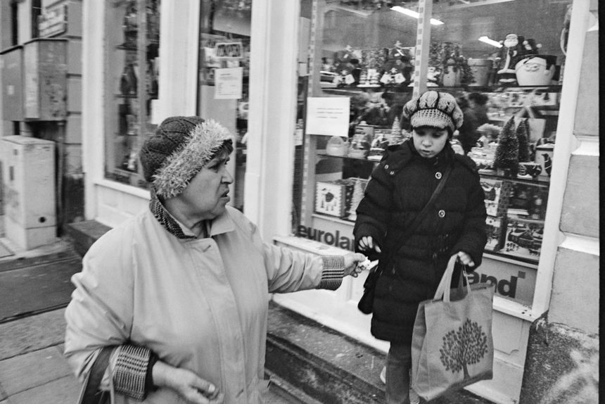 Показателен портрет на българската средна класа. Възрастна жена подава на внучката си смачкана банкнота, докато Дядо Коледа и елените надничат от витрината на магазин, дни преди Коледа.
