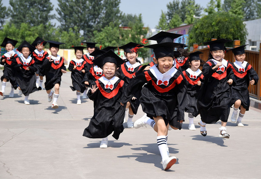 Деца, облечени с тоги и академични шапки, тичат по време на церемония за завършването на детска градина в китайската провинция Хъбей.
