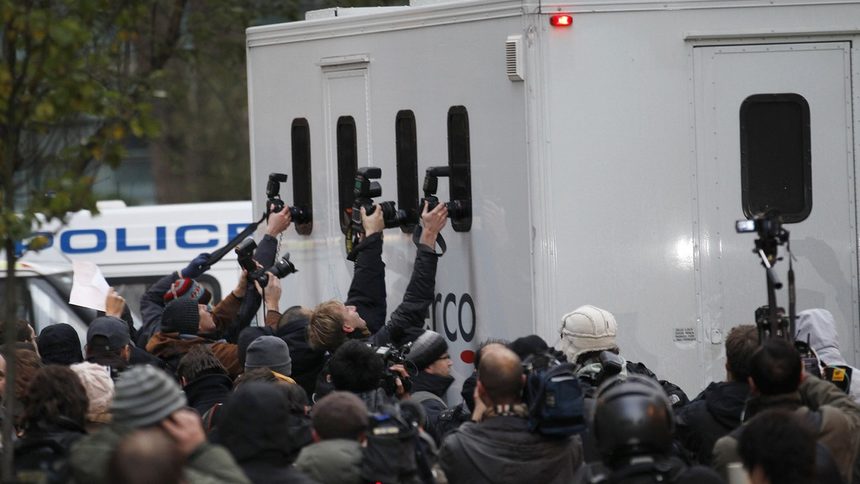 Фоторепортери опитват да снимат Асандж след ареста му в Лондон вчера.