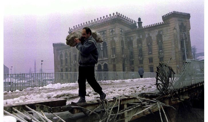 На горната снимка: мъж пренася чувал с дърва пред изгорялата сграда на библиотеката в Сараево по време на войната. Снимката е направена на 1 януари 1994 г. Долният кадър е от 4 април 2012 г.