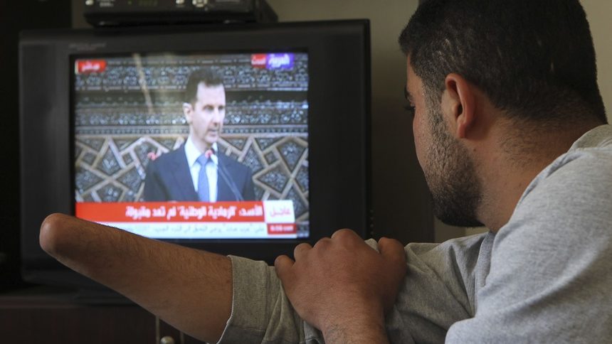 Сирийският бежанец в Йордания Захер ал Харири гледа по телевизията речта на Асад. Според Харири сирийските сили за сигурност са му отрязали ръката в болницата в Дераа, след като отишъл за помощ, защото куршум пронизал дланта му.