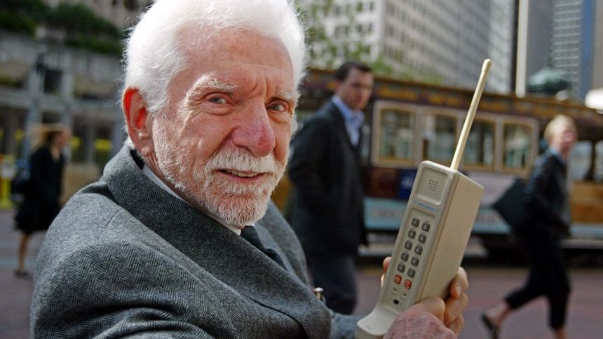 Мартин Купър на 30-та годишнина на първия разговор по мобилен телефон. В ръцете му е "Тухлата" - високият 25 см DynaTAC, съдържащ 30 платки и с батерия, която се зарежда 10 часа и издържа 35-минутен разговор.
